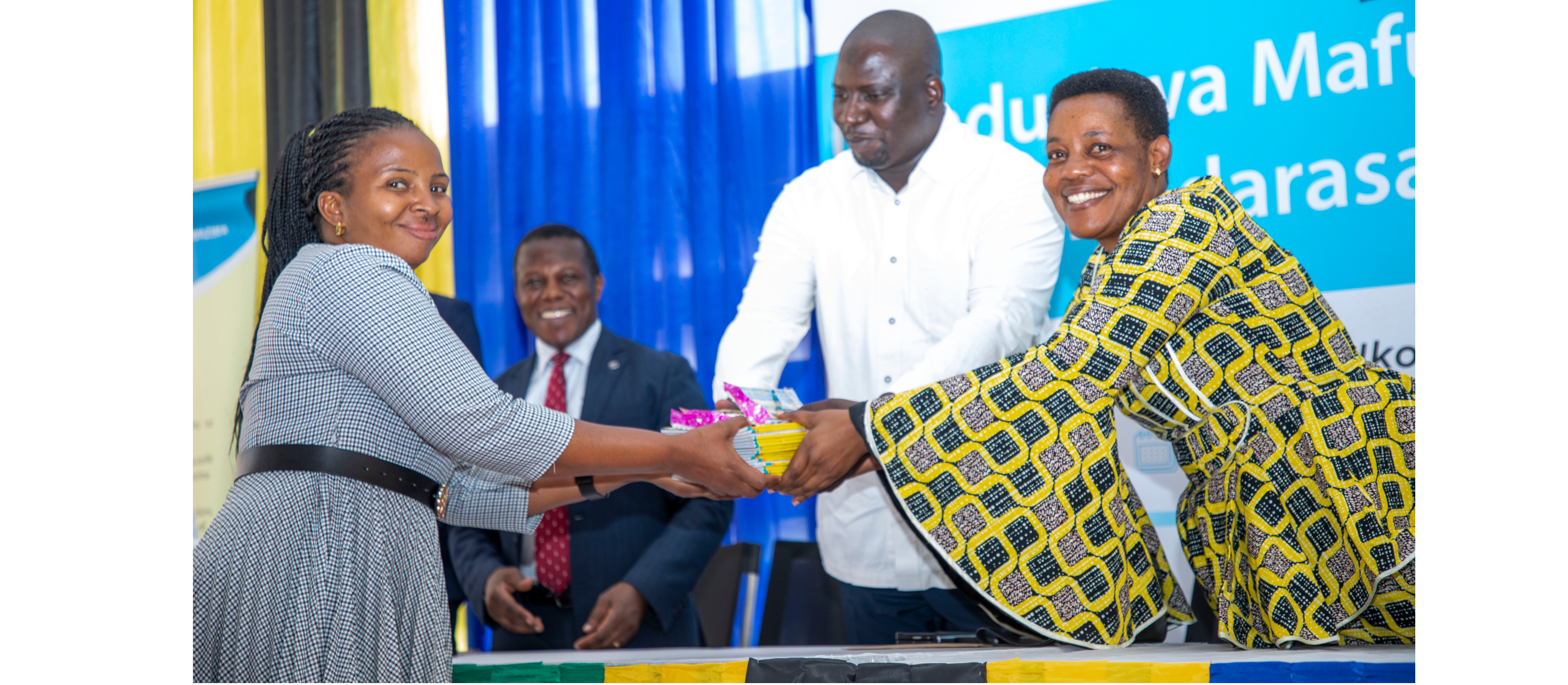 Mkuu wa Wilaya ya Urambo, Dkt. Khamisi Mkanachi (katikati), akikabidhi vitendea kazi kwa Bi. Huruma Mgoo ambaye ni mwalimu wa kituo cha kisomo Urambo...